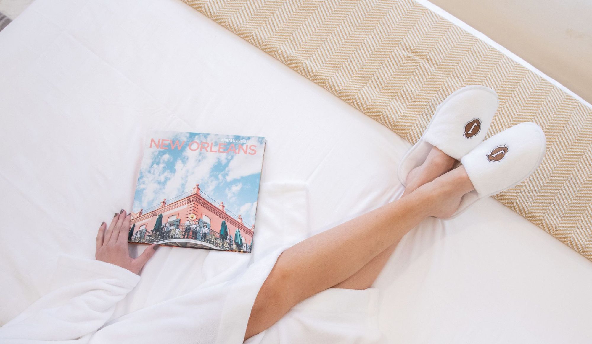 A person in a robe with slippers is lying on a bed, holding a "New Orleans" magazine.