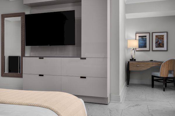 The image shows a modern room with a TV, a bed, a desk with a lamp, and artwork on the wall, creating a comfortable and stylish space.