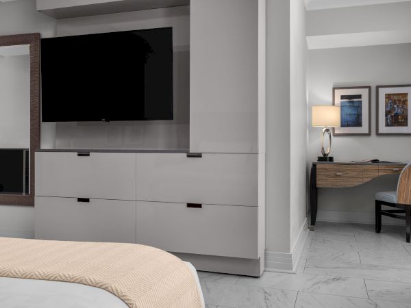 The image shows a modern room with a TV, a bed, a desk with a lamp, and artwork on the wall, creating a comfortable and stylish space.