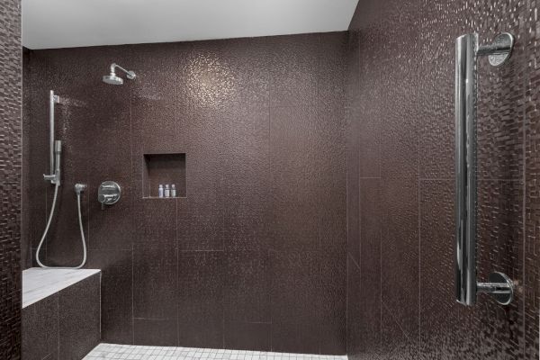 A modern shower with textured brown tiles, a bench, and built-in shelves holding small bottles.