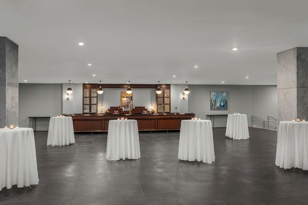 A dimly lit bar area with round tables draped in white tablecloths, candles on each table, and modern hanging lights.