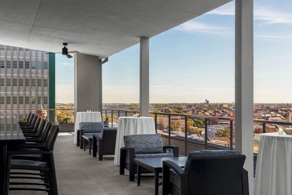 A rooftop terrace with seating, white tablecloths, and a view of the cityscape under a clear sky.