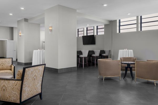 A spacious lounge with elegant seating, high tables, bar stools, and a mounted TV. Neutral tones and modern decor create a cozy ambiance.