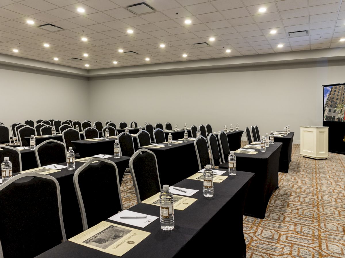 An empty conference room with rows of tables, chairs, water bottles, and notepads set up for a meeting or presentation.