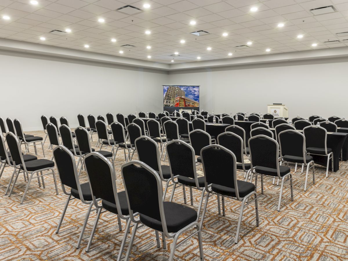 A conference room with rows of empty chairs facing a podium and screen, ready for an event or presentation.