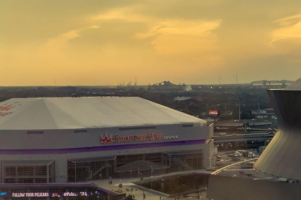 An arena is shown with a parking lot and a distinctive circular structure nearby under a cloudy sky at dusk.