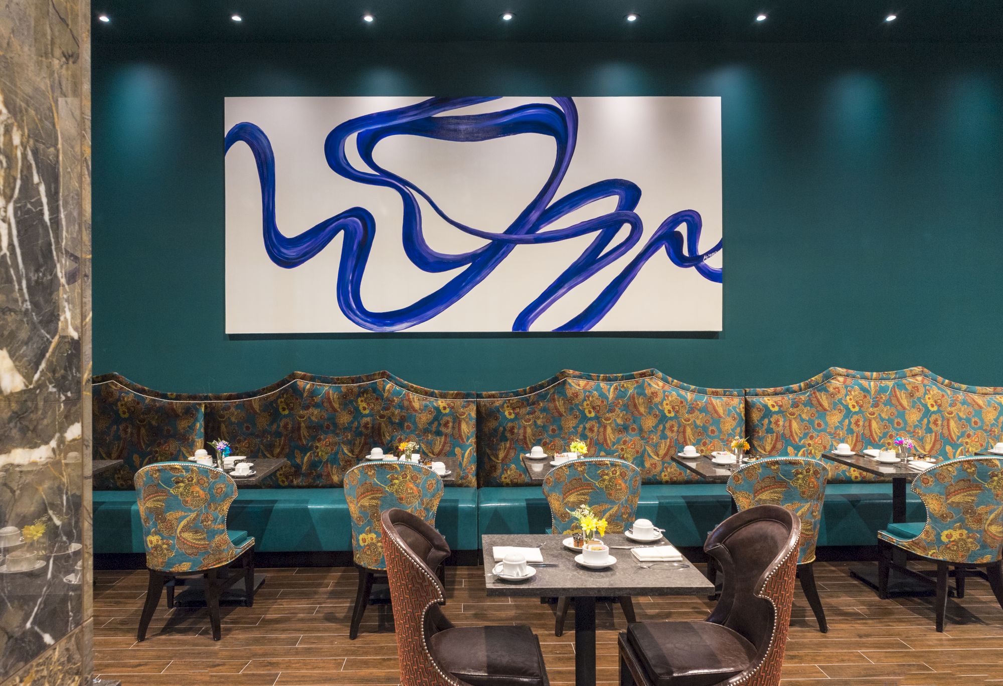 A modern dining area with colorful chairs, a patterned bench, and a large abstract painting with blue swirls on the wall.