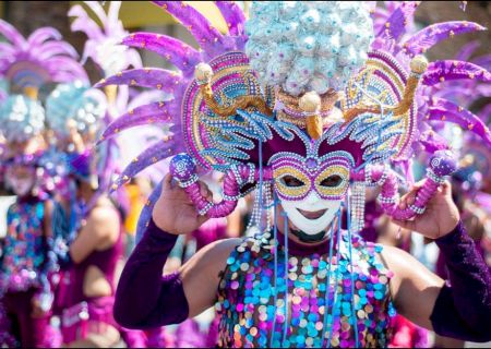 People in vibrant costumes and ornate masks with feathers and beads, participating in a colorful festival or parade.