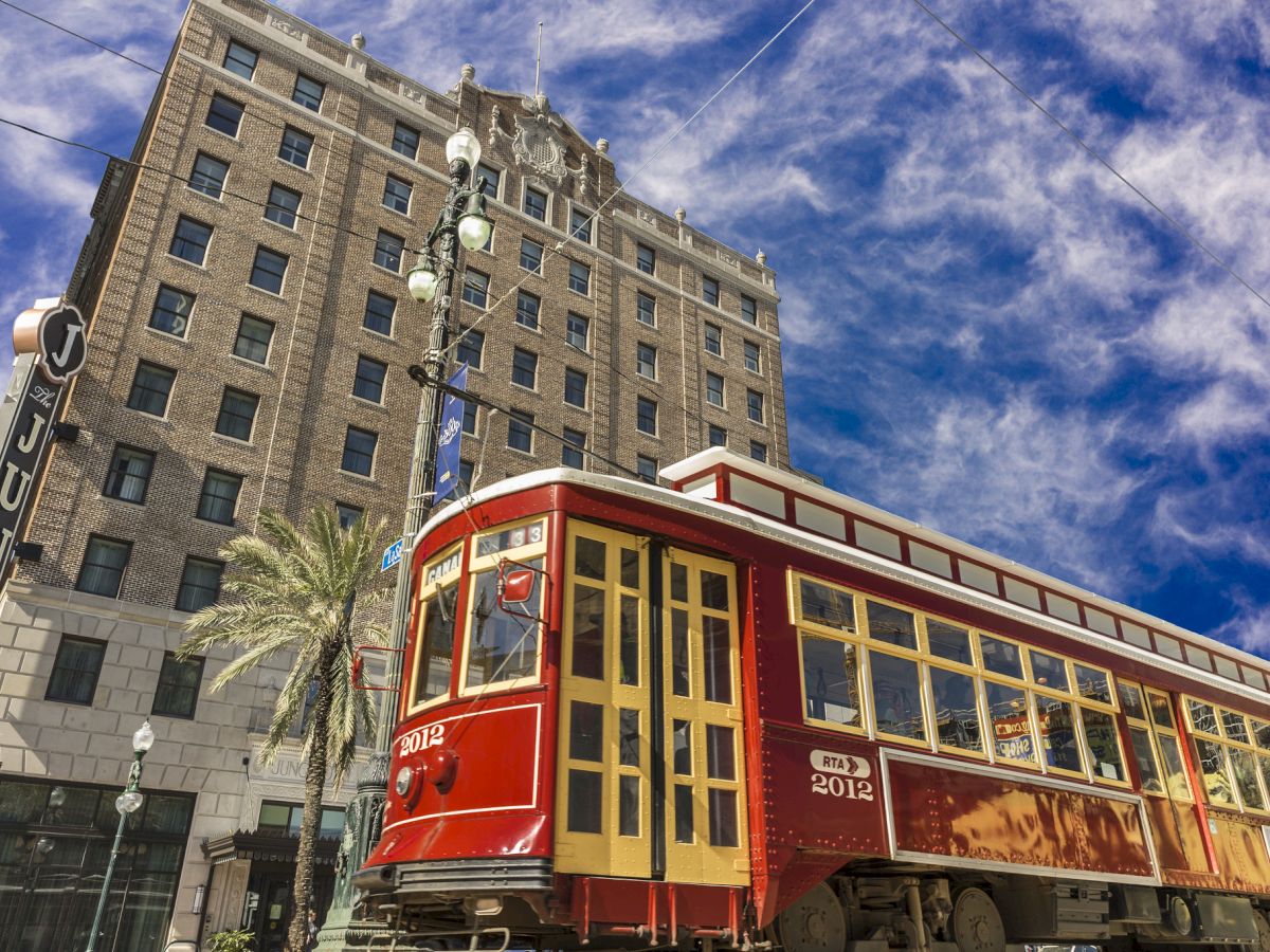 A red streetcar passes in front of a historic brick building under a vibrant blue sky.