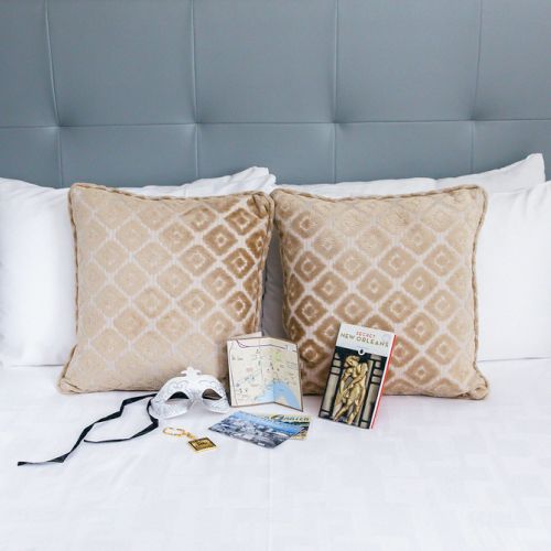 Two beige pillows on a bed with a map, book, mask, and postcards arranged in front of them.
