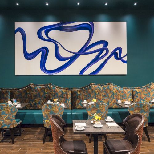 A stylish restaurant interior with patterned seating, a bold blue abstract painting, and elegantly set tables.