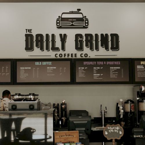 A coffee shop counter with "The Daily Grind Coffee Co." sign, menus for hot/cold coffee, teas, smoothies, and breakfast options.