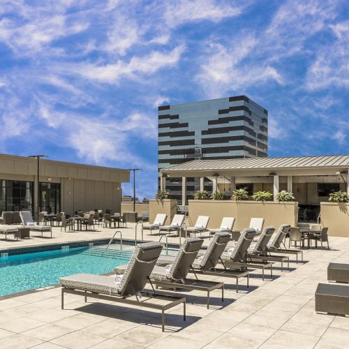 The image shows a rooftop pool area with lounge chairs and a nearby building against a sky with clouds.