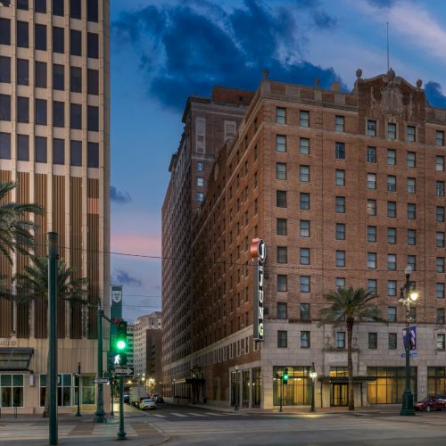 The image shows an urban street with tall buildings, palm trees, streetcars, and lit streetlamps under a cloudy sky.