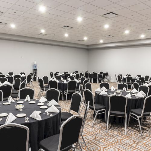 A banquet hall with multiple round tables set with tablecloths, napkins, and chairs, ready for an event.