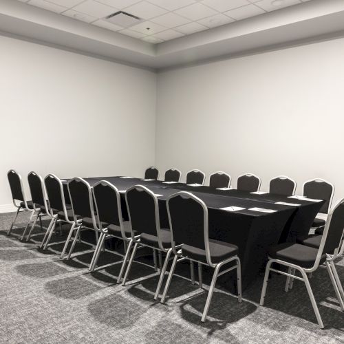 A large, empty conference room with a long table surrounded by chairs in a U-shape is shown. The room has white walls and a gray carpet.