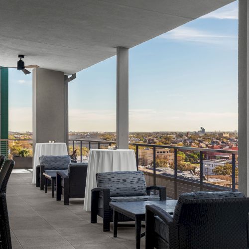 The image shows a rooftop terrace with tables, chairs, and a view of the city skyline in the distance.