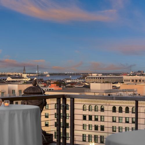 Rooftop view with candles on tables, overlooking a cityscape at sunset with clouds in the sky.