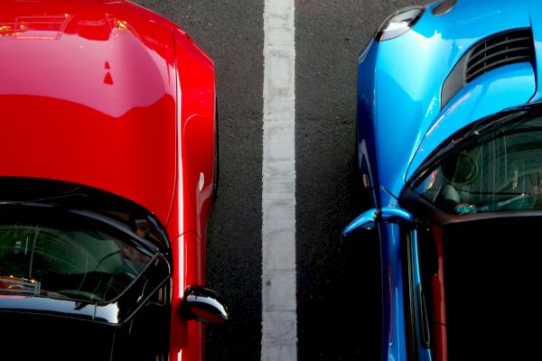 Two cars, one red and one blue, parked side by side with a white line between them, viewed from above.