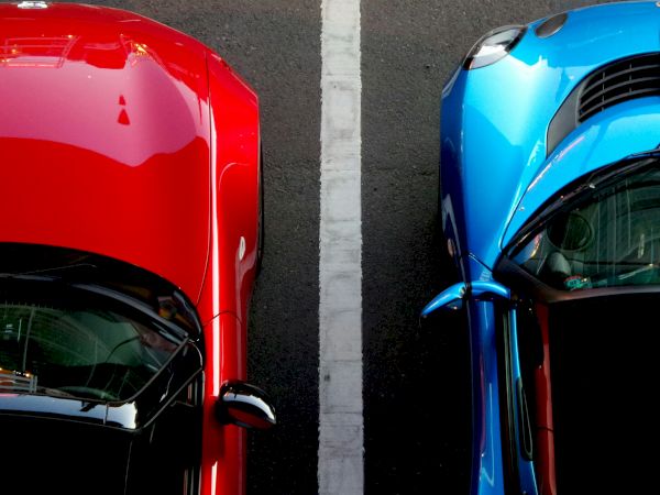 Two cars, one red and one blue, parked side by side with a white line between them, viewed from above.