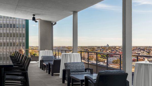 A rooftop terrace with seating, white tablecloths, and a view of the cityscape under a clear sky.