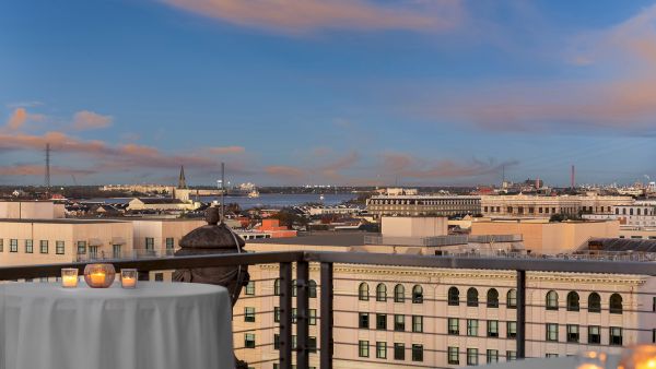A rooftop view of a cityscape with candles on tables, overlooking buildings and a river under a blue and pink sky.