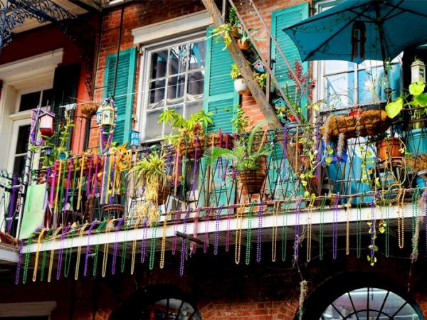 A balcony decorated with colorful beads, plants, and vibrant shutters, suggesting a festive atmosphere.