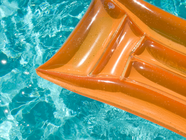 An orange inflatable kayak/float resting on clear blue swimming pool water.